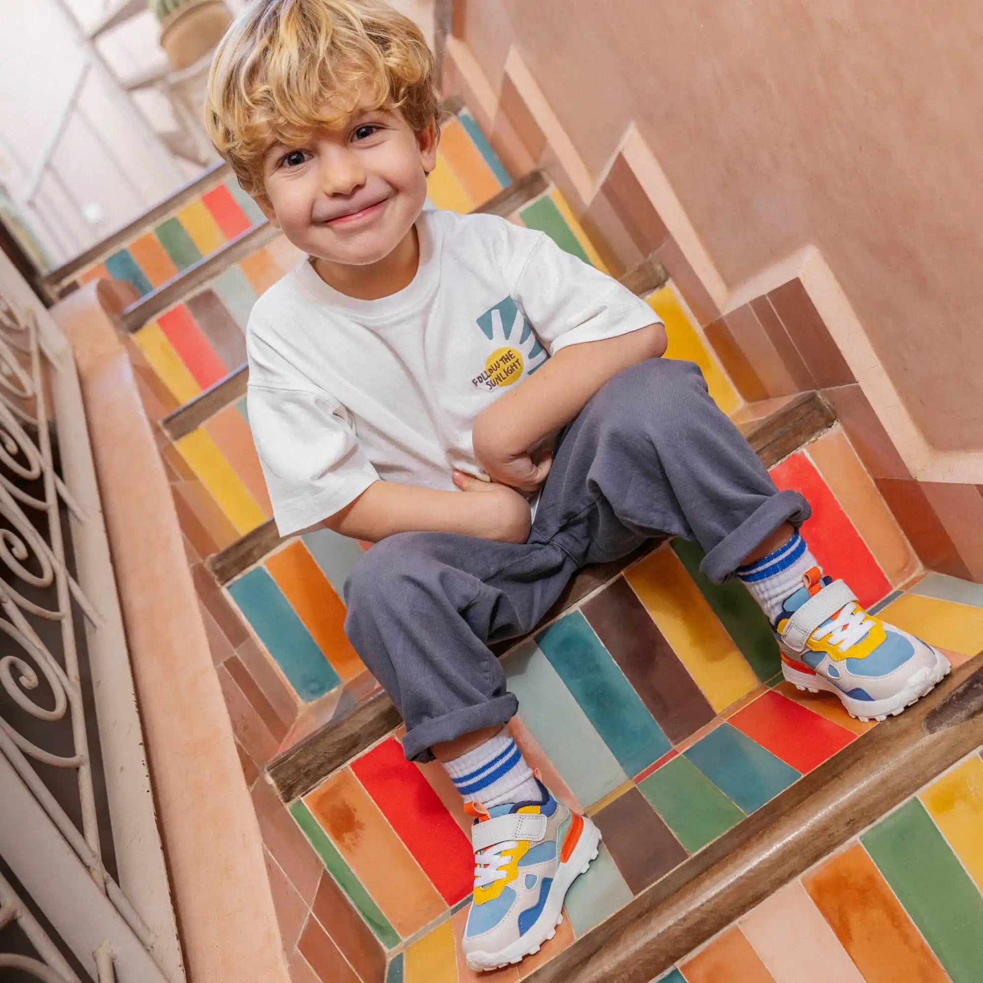 Un jeune enfant assis sur des escaliers peints de couleurs vives portant des baskets.