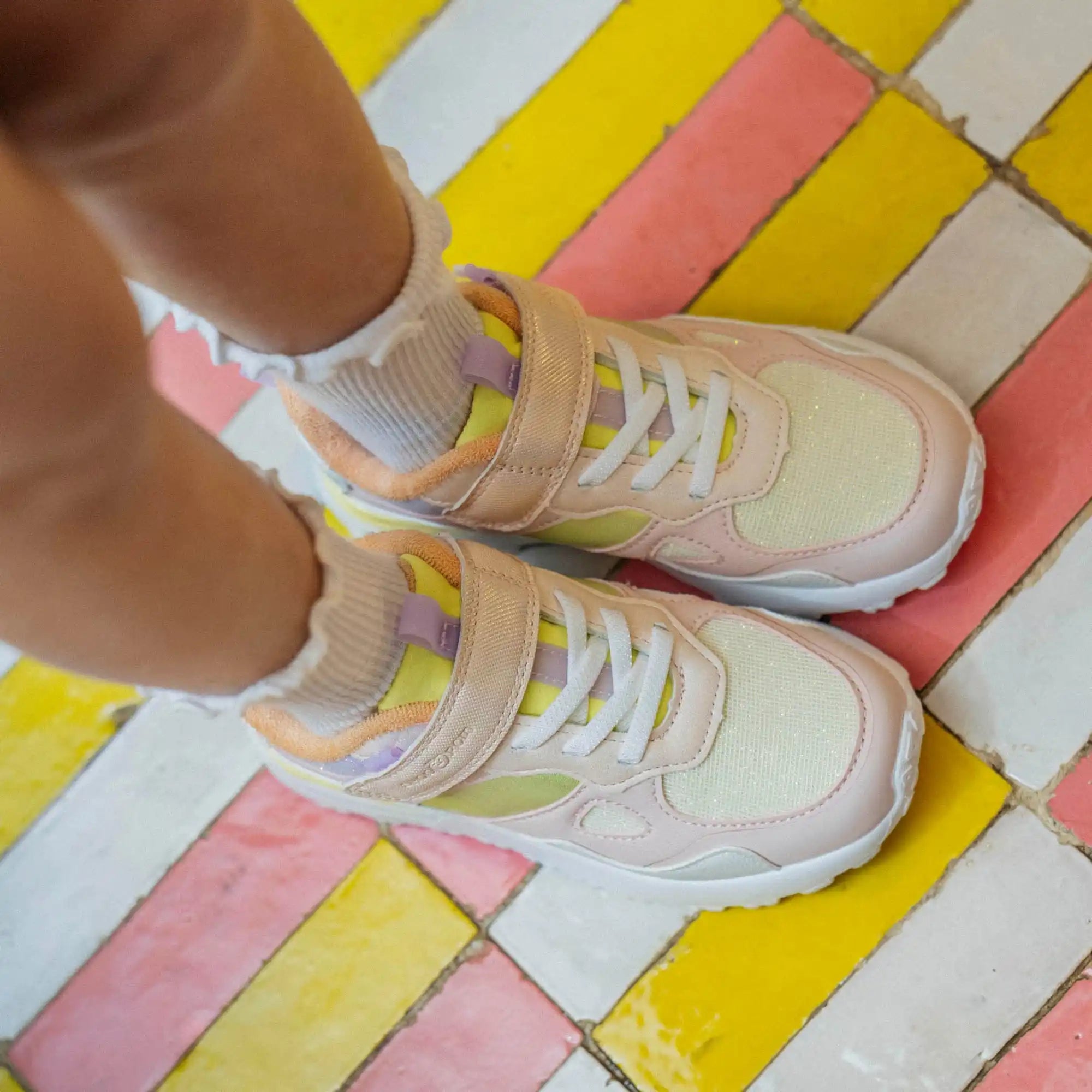 Une paire de baskets couleur crème avec des lacets blancs et une sangle auto-agrippante.